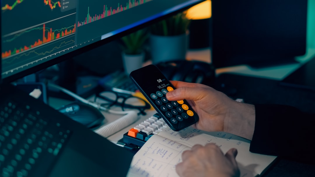 Person using calculator at desk with computer charts.